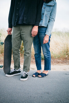 Low section of friends with skateboard standing on road