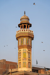 Fototapeta premium Sunset view on colorful decorated minaret of mughal era Wazir Khan mosque in the walled city of Lahore, Punjab, Pakistan with pigeons flying