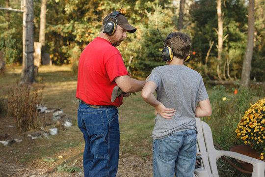 Father teaching son to shoot weapon at backyard