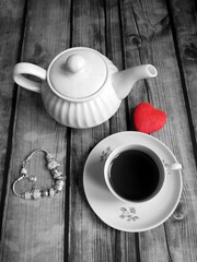 black and white image, a teapot on the table a cup of tea next to a bracelet and a small heart red color