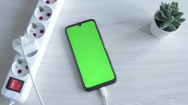 Charging mobile phone, smartphone. Man put cell phone charge on extension cord socket on wooden background. Connecting the charger USB C. Charg device process.Green screen