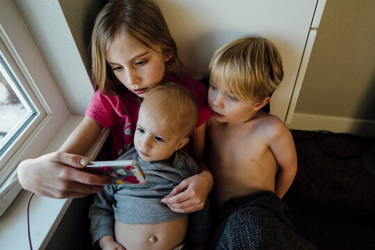 High angle view of siblings looking at mobile phone while sitting by window
