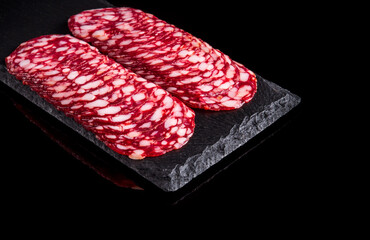 Sliced salami on a slate serving Board. Black isolated background