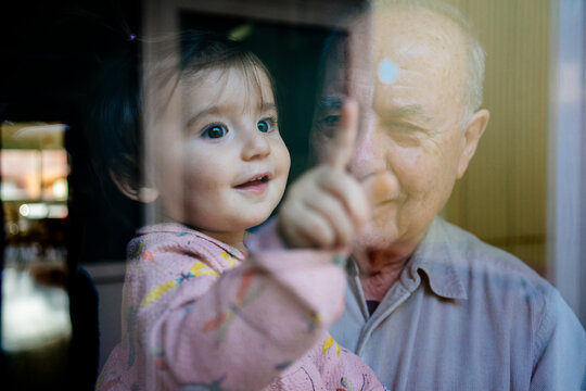 Close-up of cheerful granddaughter touching window while being carried by grandfather at home
