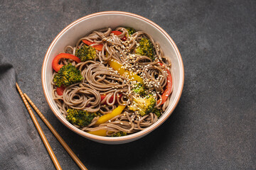 Fried buckwheat noodles with broccoli, colorful bell peppers and sesame seeds. Vegan stir fry in bowl. Healthy food 