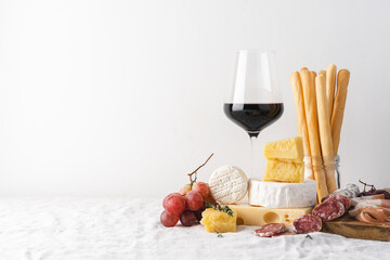 Glass of red wine and cheese, sausage, grapes and grissini bread sticks on the table. Light...