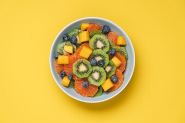Fruit salad of red oranges, kiwi, mango and berries. Bowl of fruits on yellow background 