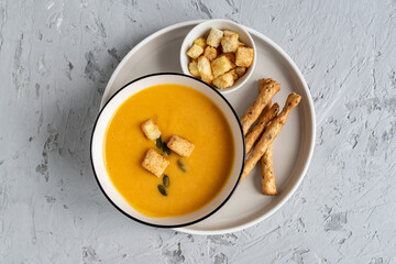 Top view of Pumpkin, carrot cream soup in a bowl. with croutons, pumpkin seeds and bread sticks.