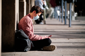 Man wearing a face mask and using a digital tablet outdoors.