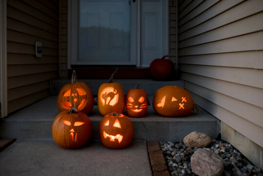 Illuminated jack o lanterns on steps in front of house at sunset - Powered by Adobe