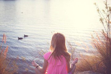 Rear view of girl meditating while sitting by lake