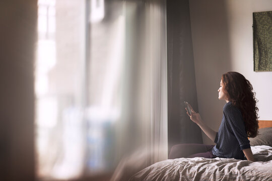 Woman using mobile phone while sitting on bed at home