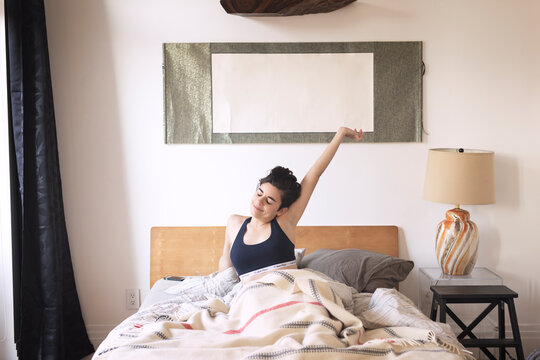 Woman stretching while waking up on bed at home