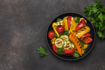Variety of grilled vegetables in bowl on black background. Zucchini, bell peppers, hot peppers, tomatoes and green parsley