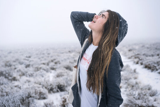 Woman with long hair looking up while standing on snow covered field
