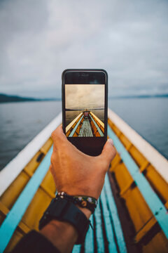 Cropped hand photographing boat through smart phone against sky