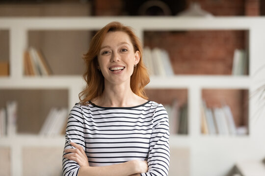 Portrait of smiling young Caucasian businesswoman pose in modern office. Happy 30s red-haired European female employee or worker show leadership and success at workplace. Recruitment concept.