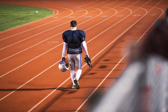 Rear view of American football player walking on sports track in stadium