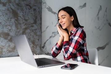 Portrait of charming woman smiling while working with laptop at home