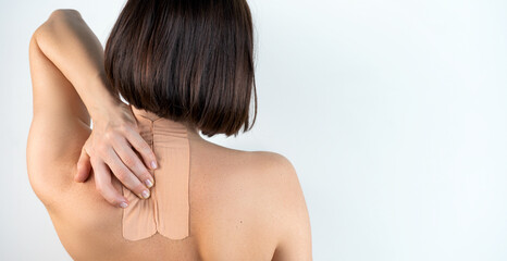 Fototapeta premium Kinesiology beige taping on the human back on a gray background with a copy space. Dynamic functional bandage taping on the girl's neck. Solution for back and neck pain. Headache.