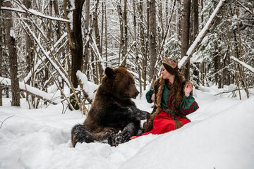 Russian beauty in folk national dress with a brown bear with a winter forest