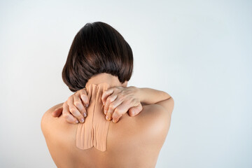Kinesiology beige taping on the human back on a gray background with a copy space. Dynamic functional bandage taping on the girl's neck. Solution for back and neck pain. Headache.
