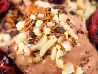 Chocolate ice cream with sprinkles, nuts and fresh cherries, closeup.