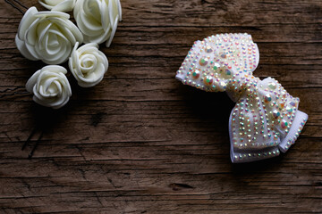 Jewelry and hair accessories. Elegant bow with holographic stones and rhinestones with a pink tint. There are cute milky roses around. Costume jewelry on an old wooden background covering