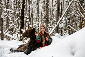 Russian beauty in folk national dress with a brown bear with a winter forest