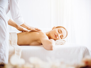 Obraz na płótnie Canvas Beautiful woman enjoying back massage with closed eyes in sunny spa center. Relaxing treatment concept in medicine