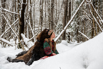 Russian beauty in folk national dress with a brown bear with a winter forest