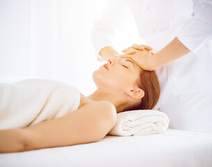 Fototapeta na wymiar Beautiful woman enjoying facial massage with closed eyes in sunny spa center