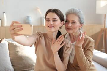 Happy middle aged mother and daughter taking selfie at home.