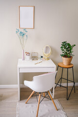 Minimalistic female still life workplace interior pastel colors. White table chair empty poster mock up frame, stylish fashion accessories golden mirror. Home plant in eco wicker flower pot. Template