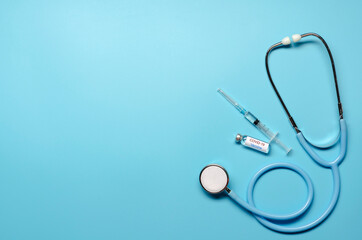 Ampoule with vaccine of COVID-19, syringe and stethoscope on blue background. Flat lay with copy space