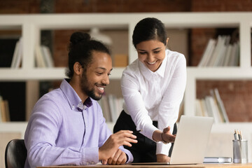 Happy diverse young multiracial businesspeople brainstorm work together on laptop in office. Smiling multiethnic colleagues coworkers look at computer screen cooperate. Teamwork concept.