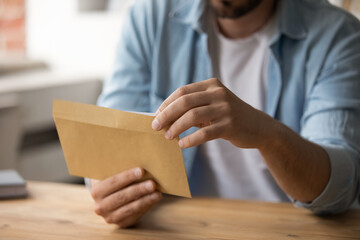 Crop close up of man sit at desk hold open envelope with postal letter or correspondence. Male employee receive post paperwork document or paper notice or mail. Invitation, bank invoice concept. - obrazy, fototapety, plakaty