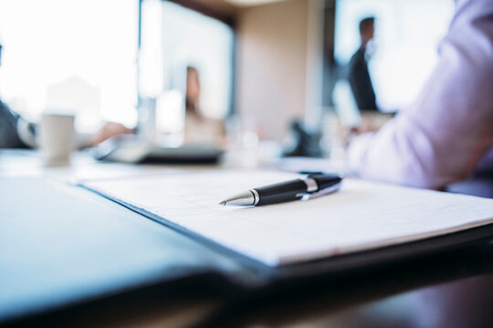 Close-up of pen and document on table with business people in background
