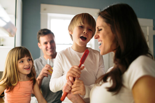 Family looking at woman singing with spatula in kitchen