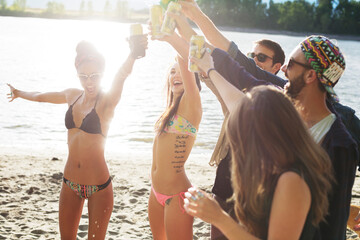 Cheerful friends toasting cans while enjoying at riverbank
