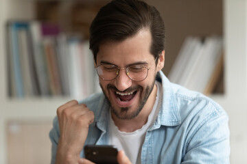 Close up of excited young Caucasian man look at smartphone screen triumph win lottery online....