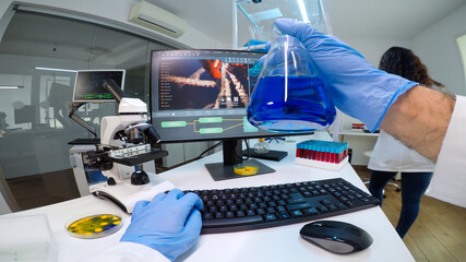 POV of scientist doctor doing research checking liquid from chemical container working in equipped laboratory. Team of researchers examining vaccine evolution using high tech chemistry tools