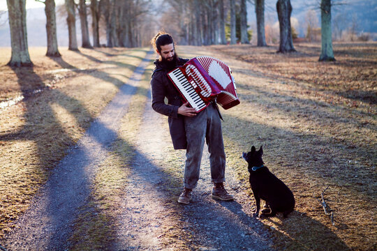 Full length of man playing accordion while dog sitting on field during vacation