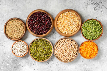 Different legumes. Mung beans, red and white beans, lentils, peas and chickpeas in wooden bowls on the light grey kitchen table. Top view