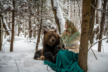 Russian beauty in folk national dress with a brown bear with a winter forest 