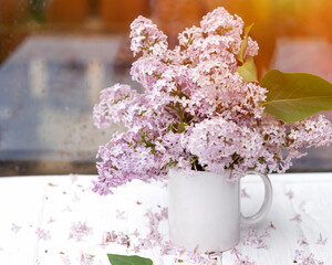 A white Cup with lilac on a vintage wooden surface on spring raining day. View from outside.