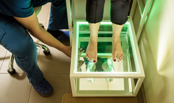 Doctor is at examining womans feet by using plantoscopy device