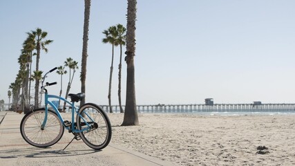 Blue bicycle, cruiser bike by sandy ocean beach, pacific coast near Oceanside pier, California USA. Summertime vacations, sea shore. Vintage cycle, tropical palm trees, lifeguard tower watchtower hut