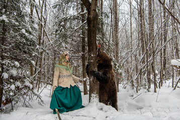 Russian beauty in folk national dress with a brown bear with a winter forest 