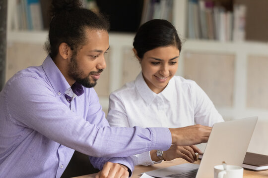 Smiling Multiracial Diverse Businesspeople Look At Laptop Screen Brainstorm Cooperate At Office Meeting. Happy Young Multiethnic Colleagues Work Together On Computer. Teamwork, Diversity Concept.